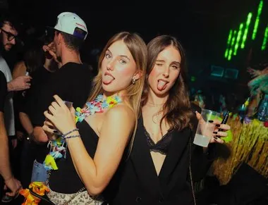 Due amiche con collane di fiori fanno la linguaccia