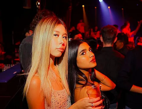 Due ragazze con i drink tra luci rosse e blu